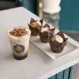 An iced fall latte beside three fall cupcakes in brown tulip liners